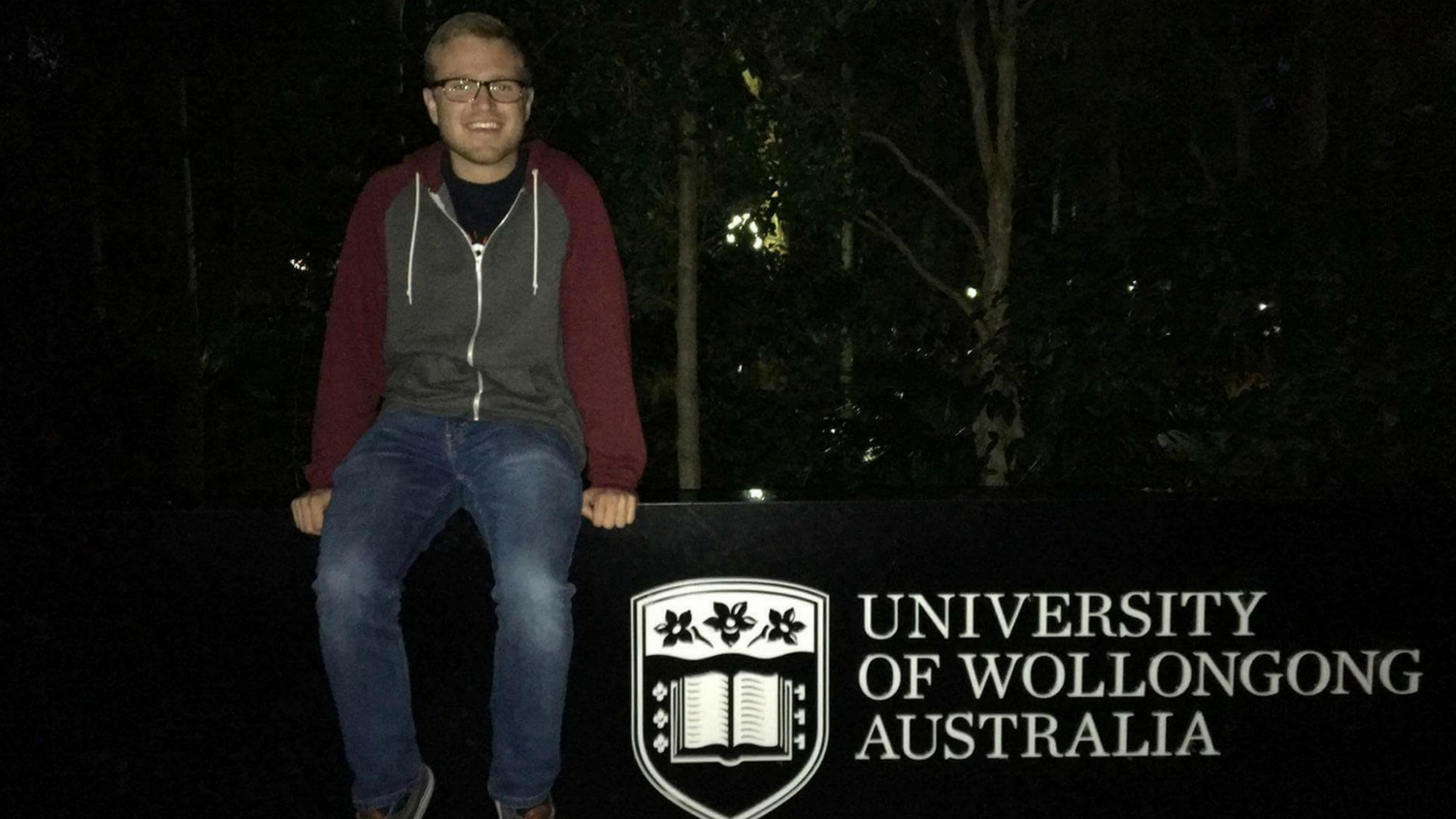 Male student sitting on University of Wollongong Australia sign