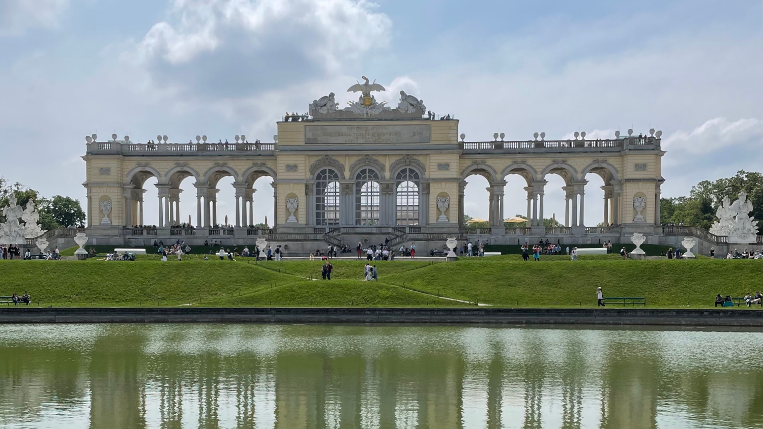 There is a view of a manmade lake and behind there is an ornate building. This is located somewhere in Austria.