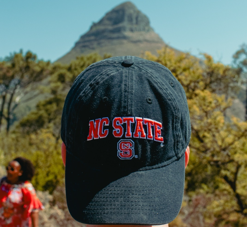 Student holding NC State hat in front of mountain